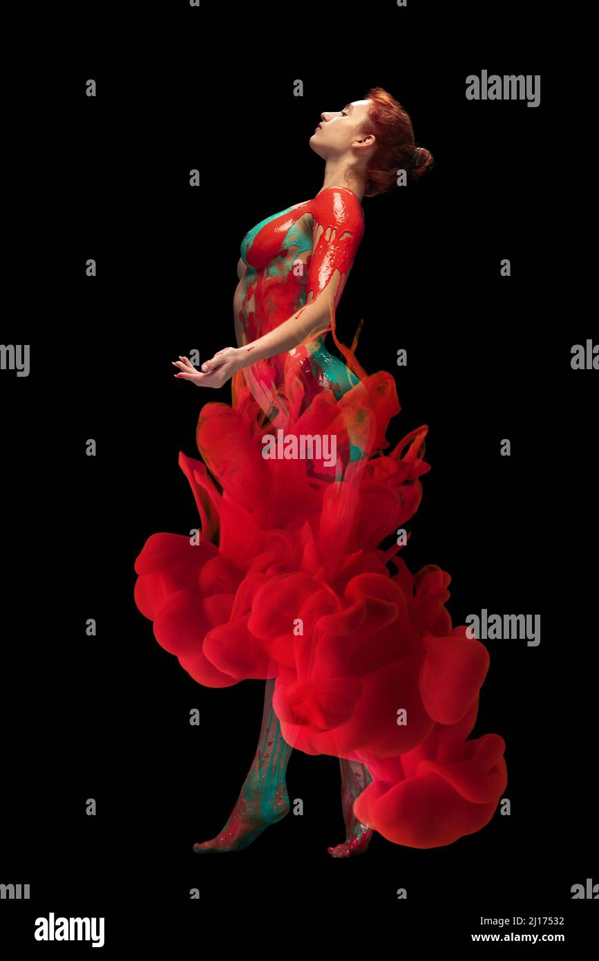 Ritratto di giovane donna tenera coperto di vernice rossa e verde e danzante splah colorante isolato su sfondo nero Foto Stock