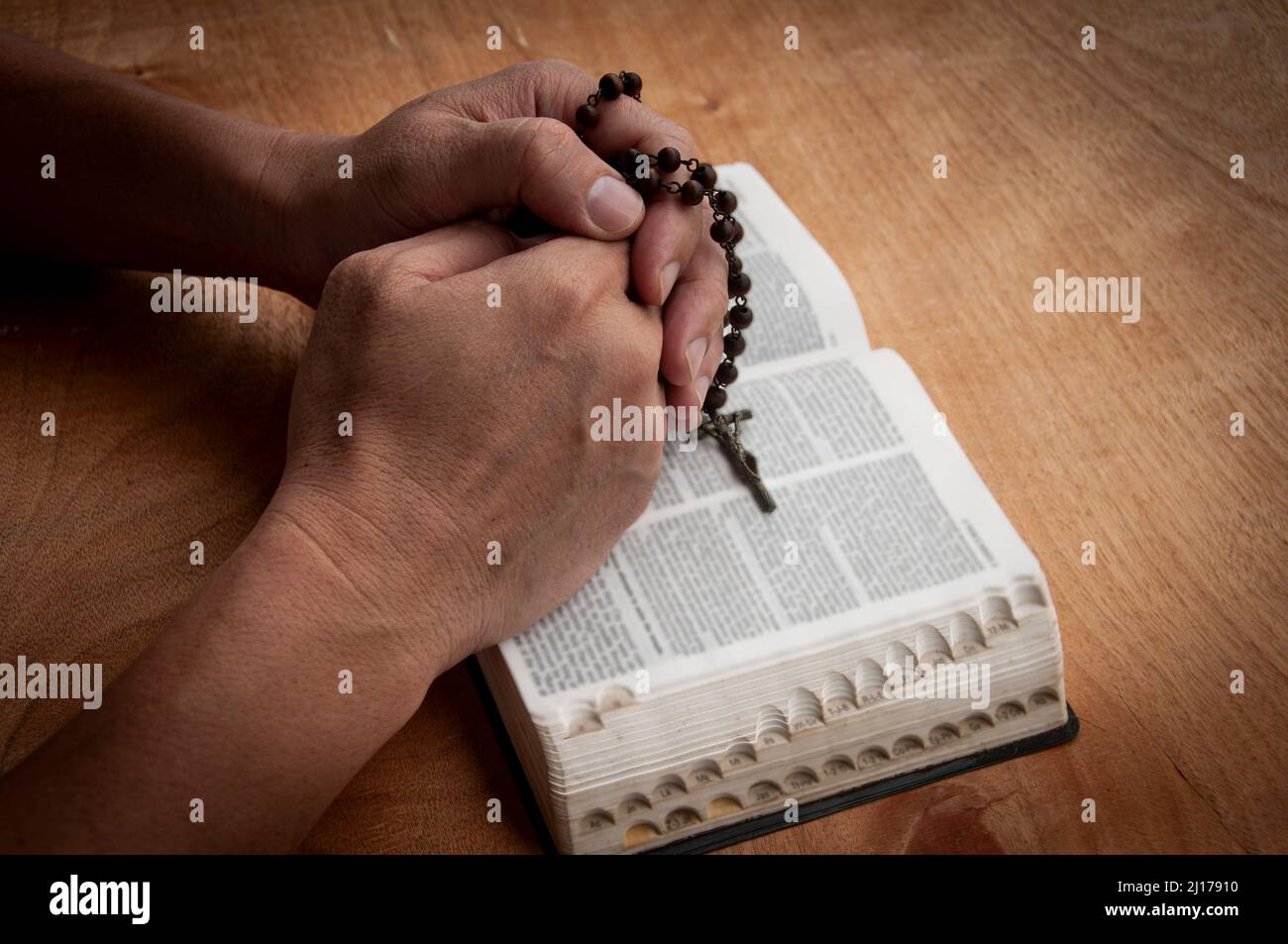 Mano che tiene Rosario su una Sacra Bibbia che prega. Concetto di cristianesimo. Foto Stock