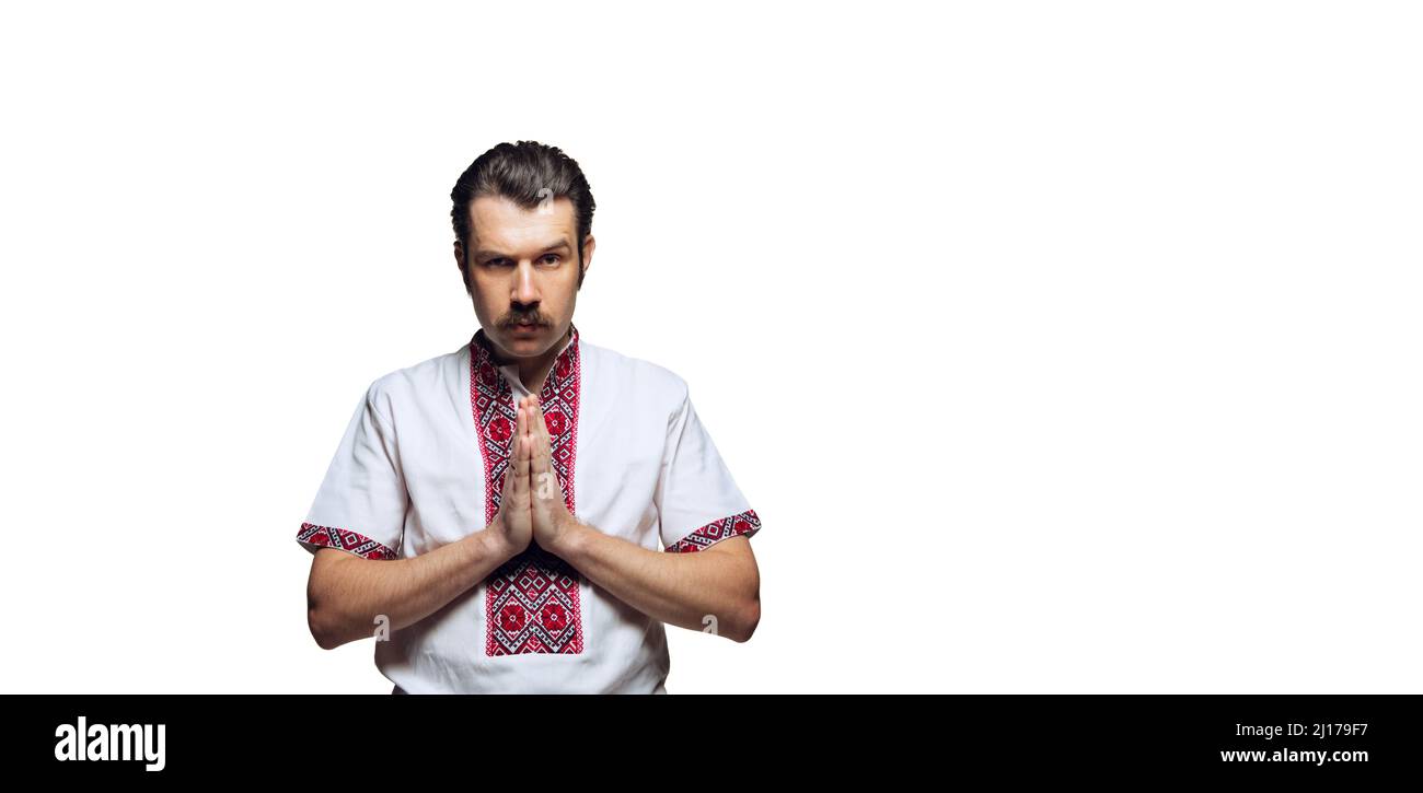 Ritratto di uomo serio che prega, indossando tessuto nazionale ucraino - camicia da ricamo isolato su sfondo bianco studio. Concentrazione Foto Stock