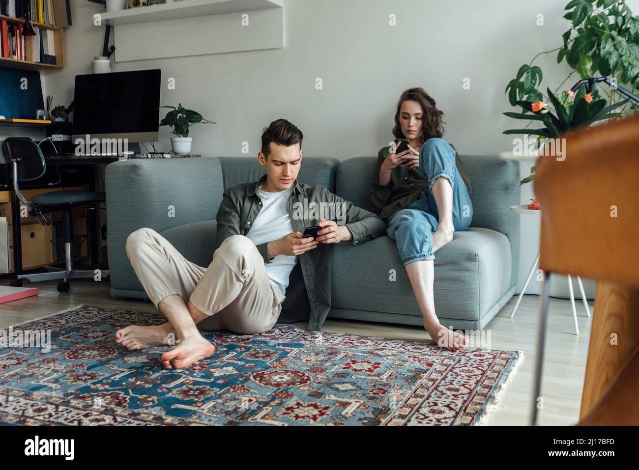 Giovane coppia che usa gli smartphone nel soggiorno di casa Foto Stock