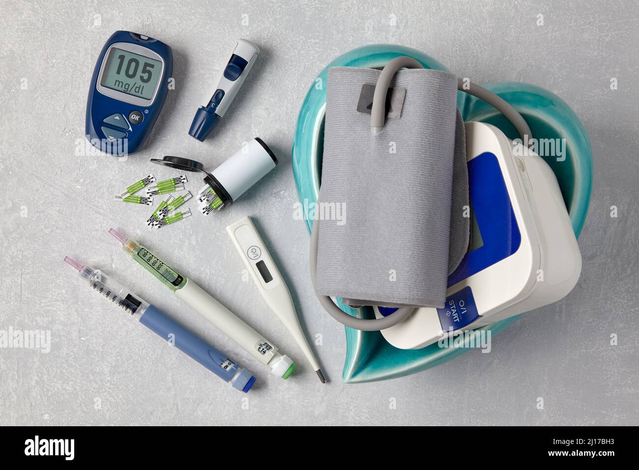 Glucometro, siringhe a penna per insulina, termometro e misuratore della  pressione sanguigna in un recipiente blu a forma di cuore su un tavolo di  cemento grigio chiaro. Medico Foto stock - Alamy