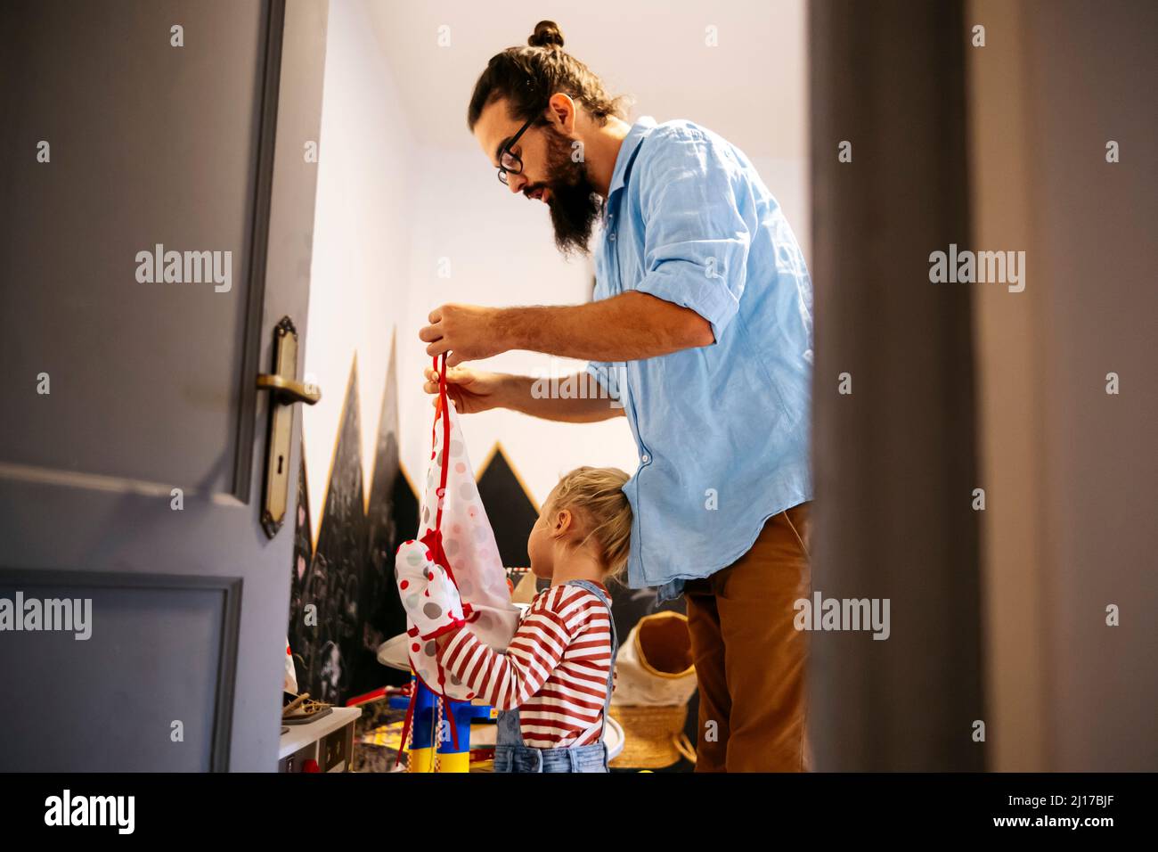 Padre che aiuta il figlio a mettere sul grembiule a casa Foto Stock