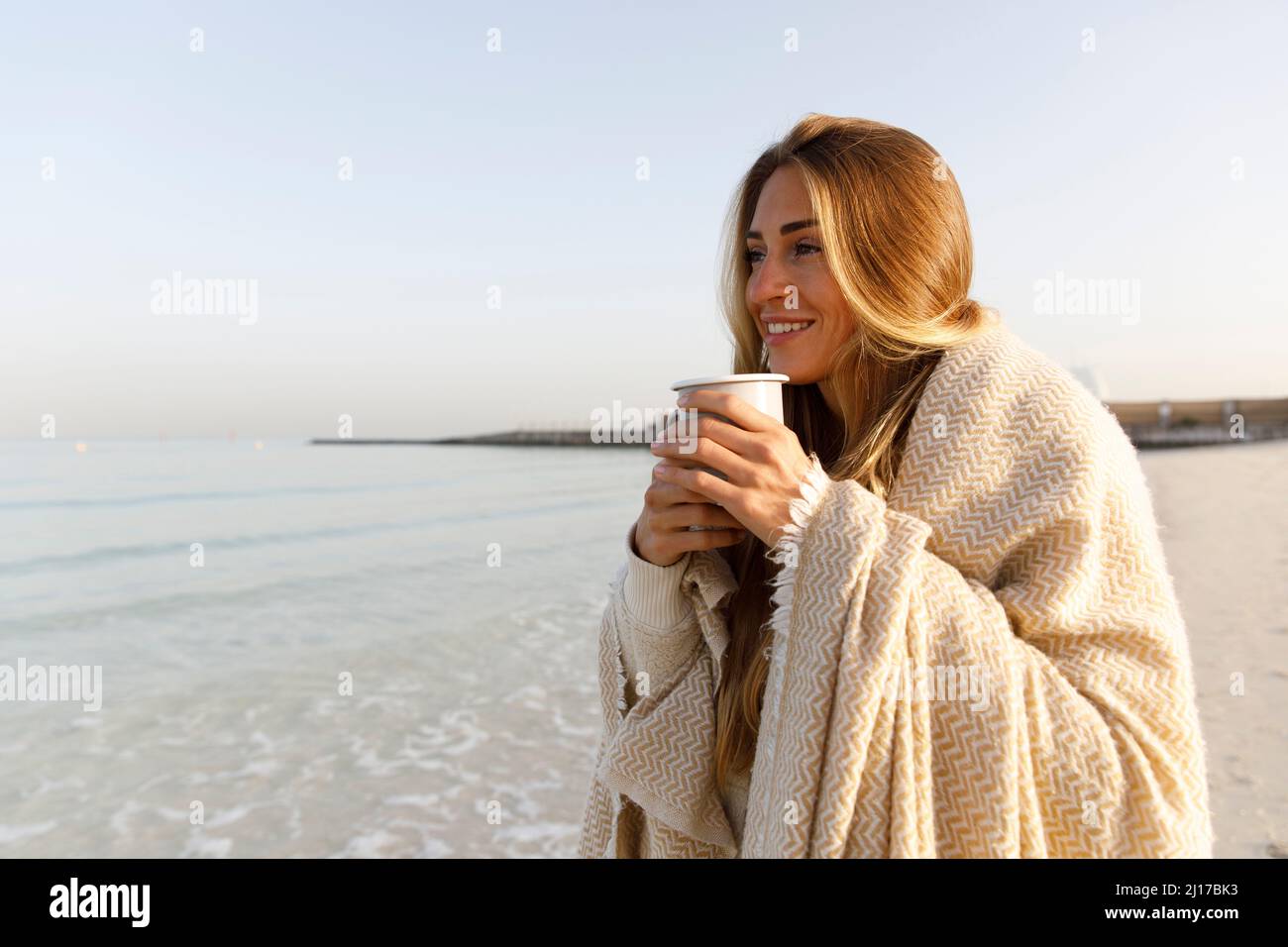 Donna felice bionda che beve il tè in spiaggia Foto Stock