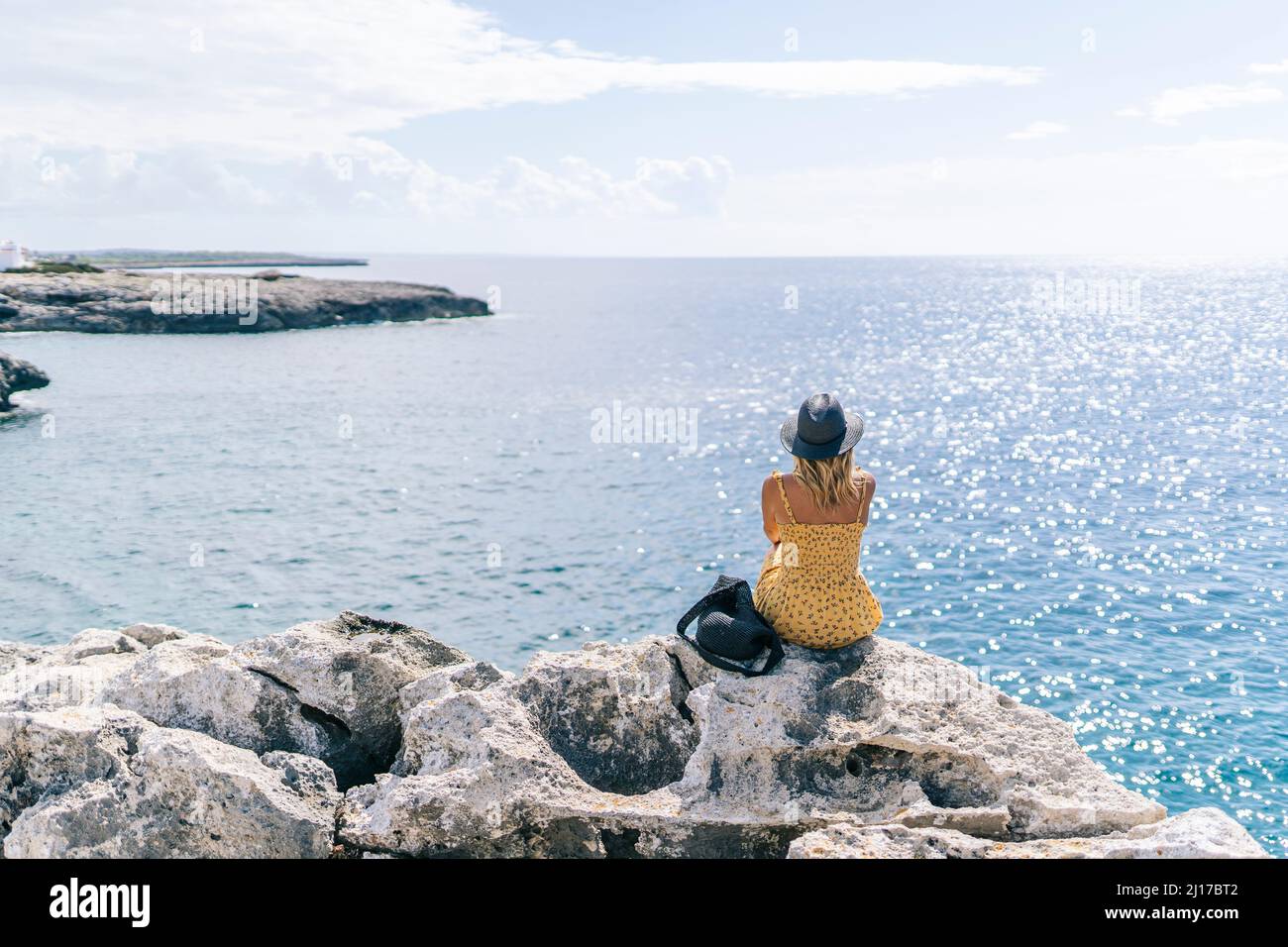 Donna seduta su roccia guardando il mare in giornata di sole, Minorca, Spagna Foto Stock