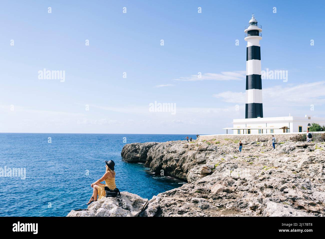 Donna seduta su roccia guardando il mare in giorno di sole, Artrutx faro, Minorca, Spagna Foto Stock