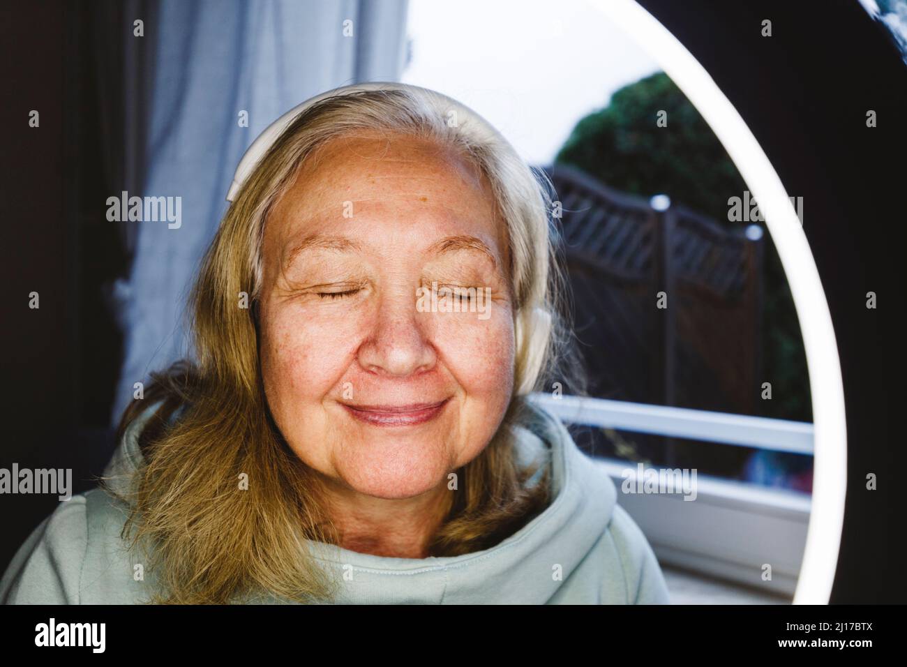 Donna anziana con occhi chiusi, vista attraverso la luce ad anello illuminata Foto Stock