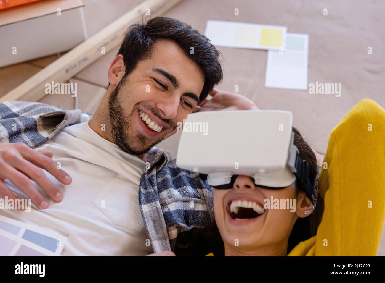 Donna felice con occhiali VR sdraiati dal ragazzo in casa di lavoro di ristrutturazione Foto Stock
