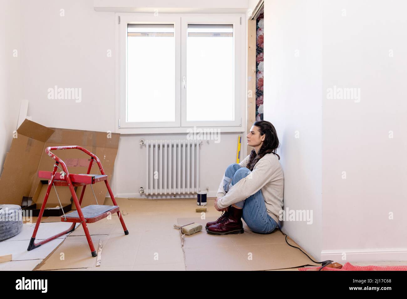 Donna pensierosa seduta sul pavimento a casa lavori di ristrutturazione Foto Stock