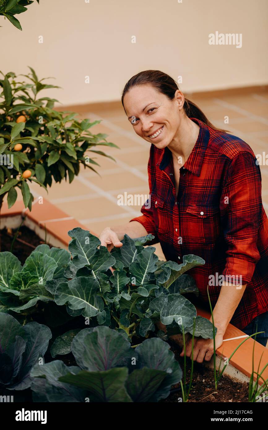 Donna felice che tocca piante fresche di broccoli nel giardino del cortile Foto Stock