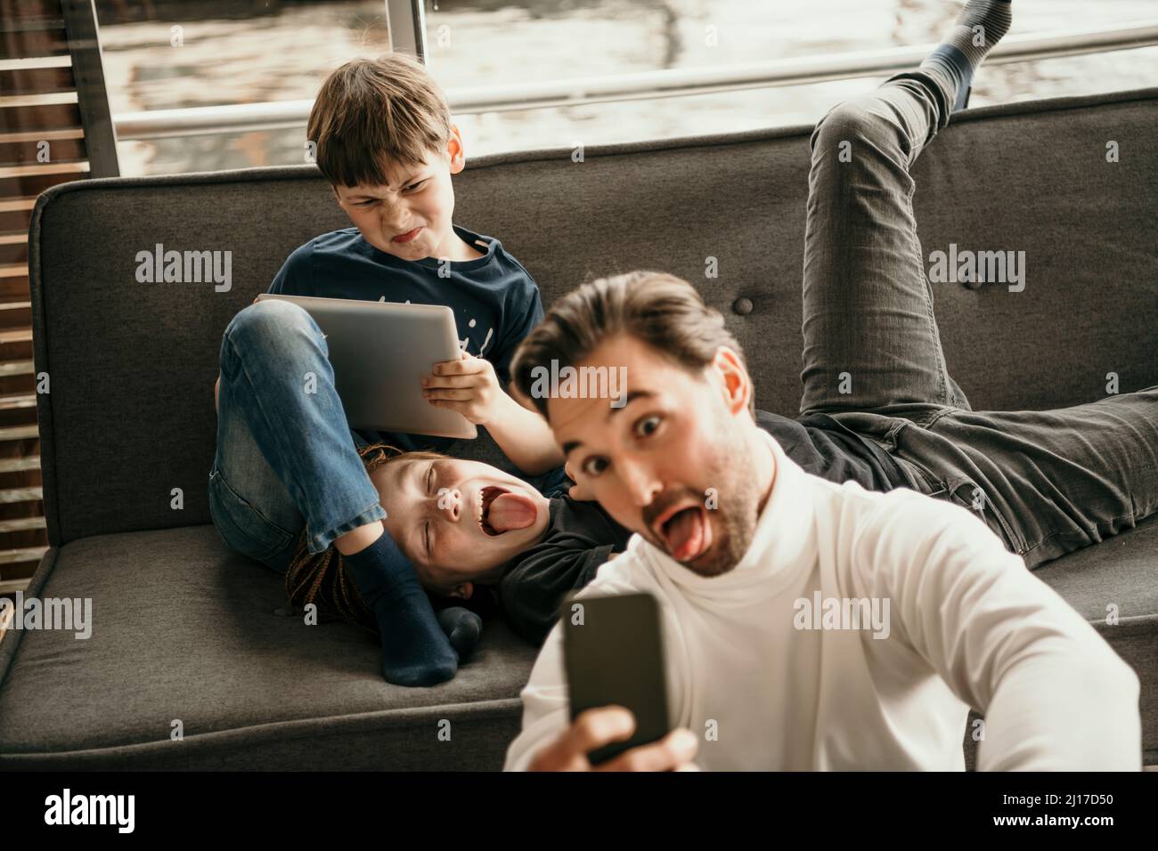 L'uomo che attacca la lingua che prende selfie con i figli che fanno i volti a casa Foto Stock