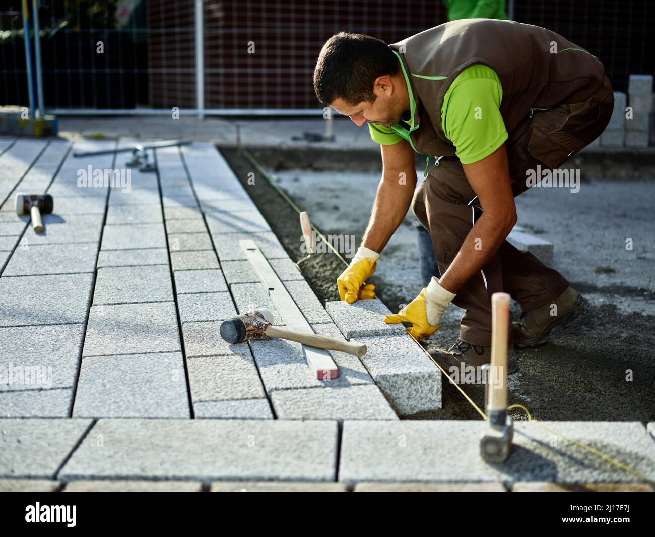 Addetto alle costruzioni che dispone le pietre di pavimentazione sul marciapiede Foto Stock