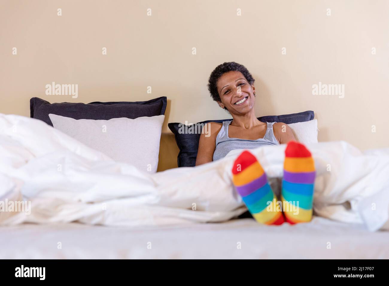 Donna sorridente con calzini multicolore seduti sul letto di casa Foto Stock