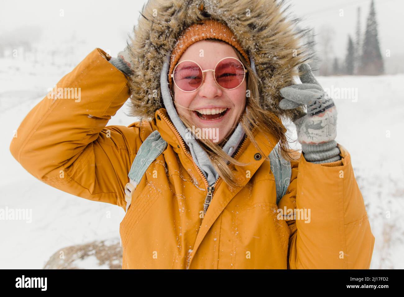 Donna felice in occhiali da sole e giacca in pelliccia godendo nella neve Foto Stock