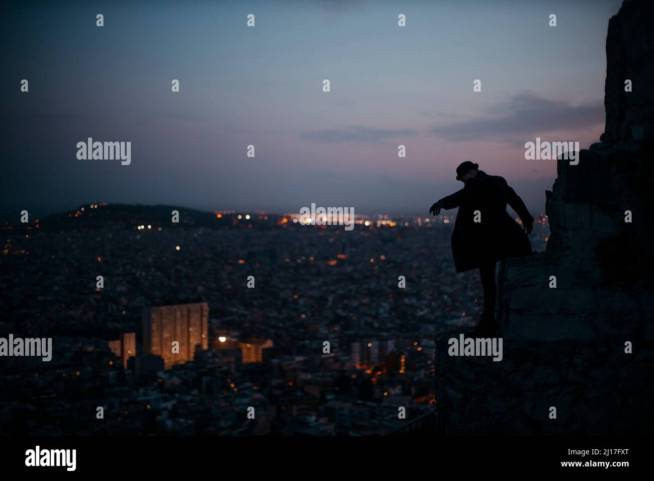 Uomo in piedi sulla roccia di fronte alla città al tramonto Foto Stock