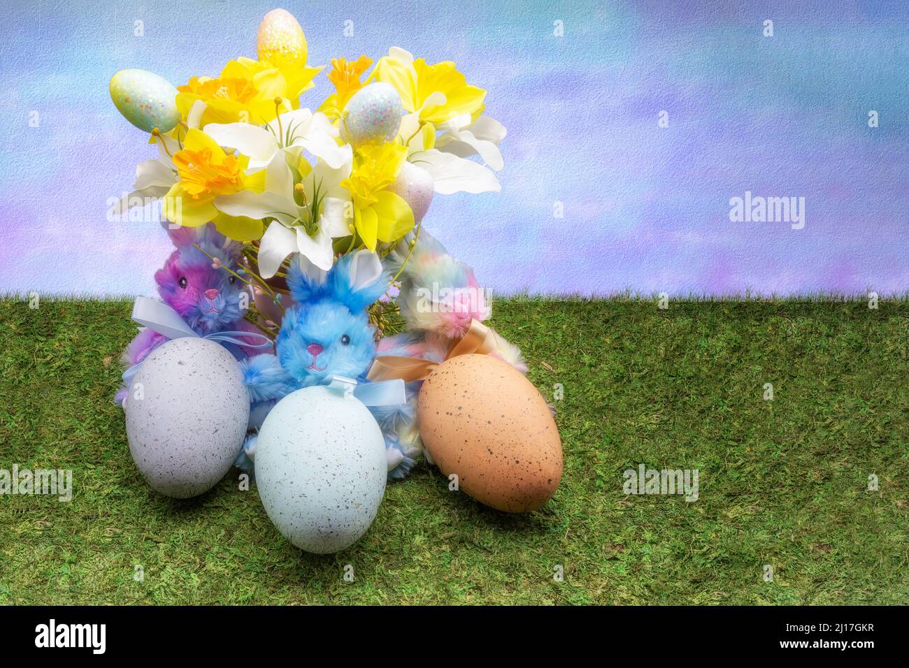 Coniglietti ripieni che tengono tre grandi uova seduti sotto un bouquet di fiori primaverili. Foto Stock