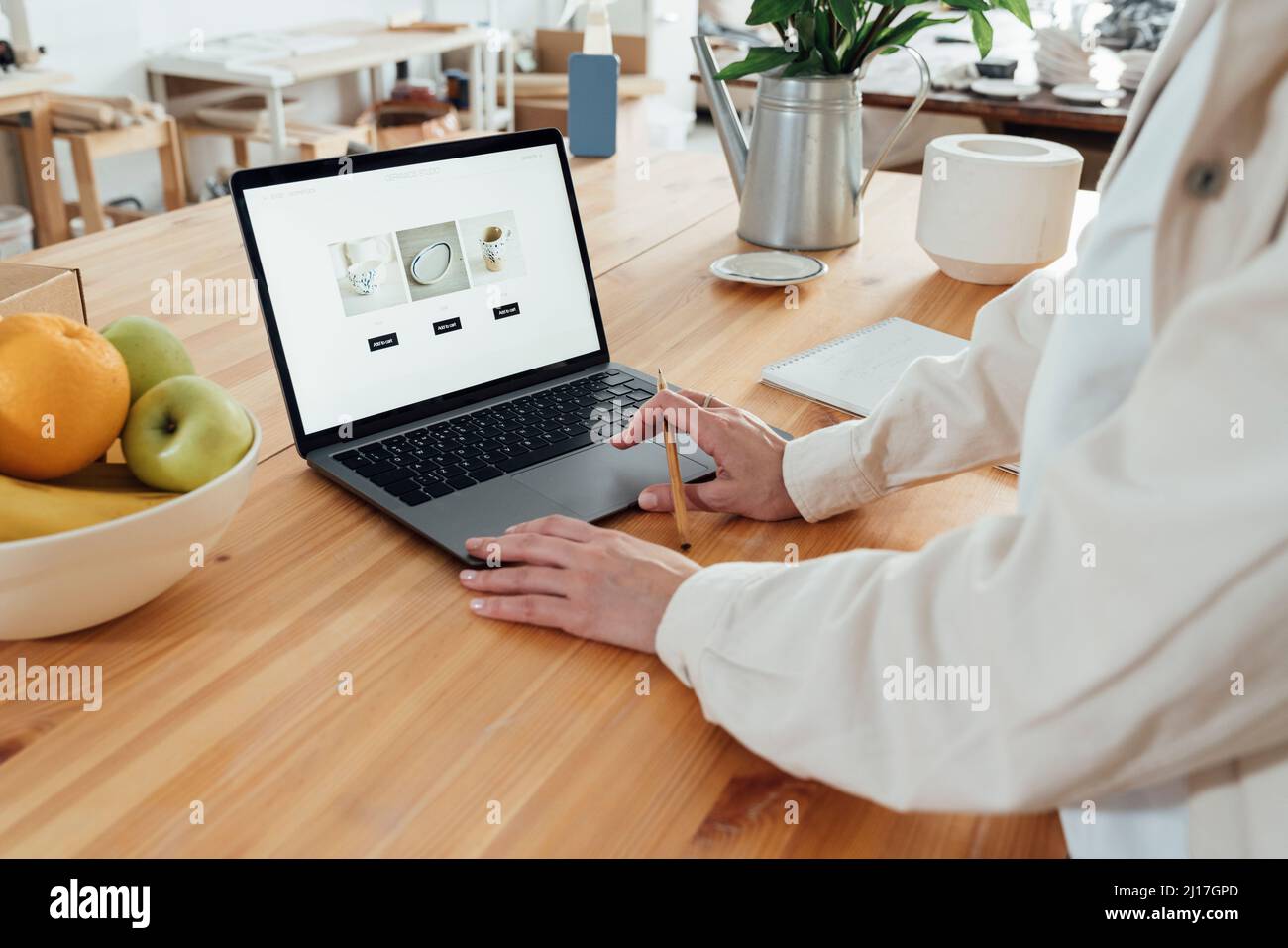 Donna che crea una pagina web per la ceramica su laptop in officina Foto Stock