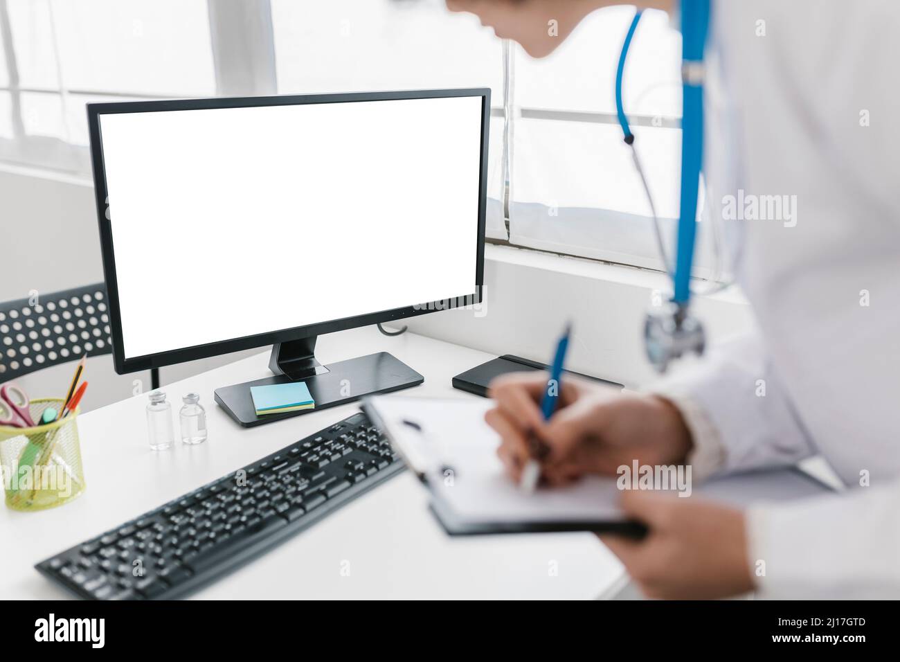 Il medico scrive sugli appunti mentre osserva lo schermo del computer alla clinica Foto Stock