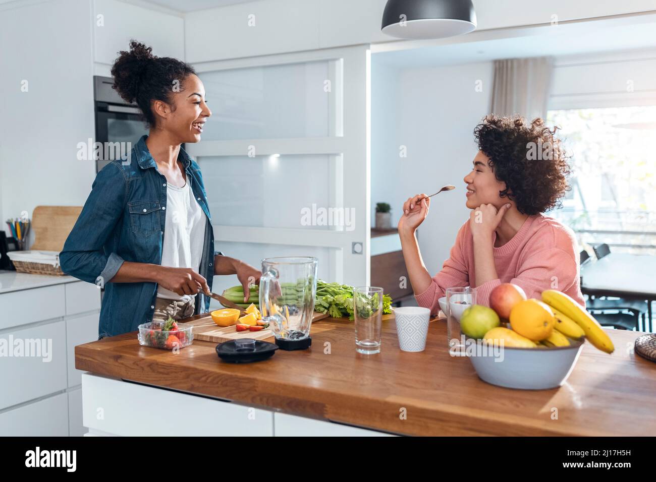 Giovane donna che parla con un amico tagliando frutta in cucina Foto Stock