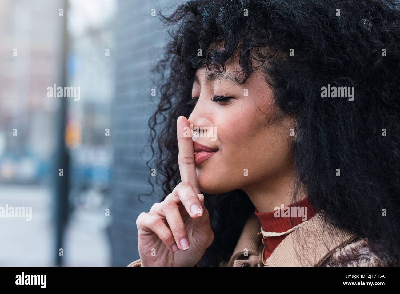 Bella donna con occhi chiusi gesturando il dito sulle labbra Foto Stock