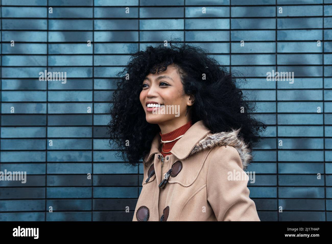 Giovane donna felice con capelli ricci di fronte alla parete blu Foto Stock