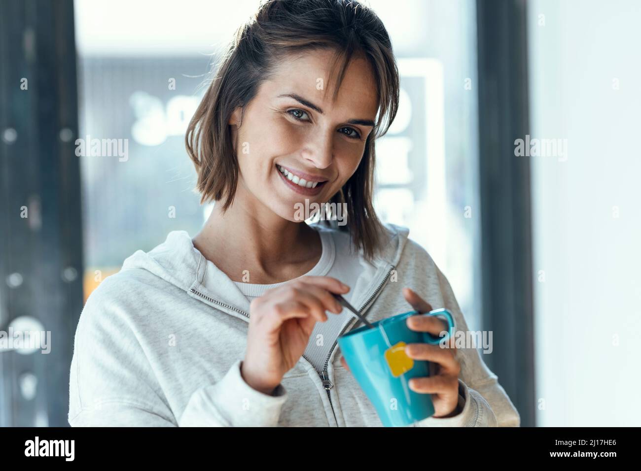 Donna sorridente che mescola il tè con un cucchiaio in tazza Foto Stock