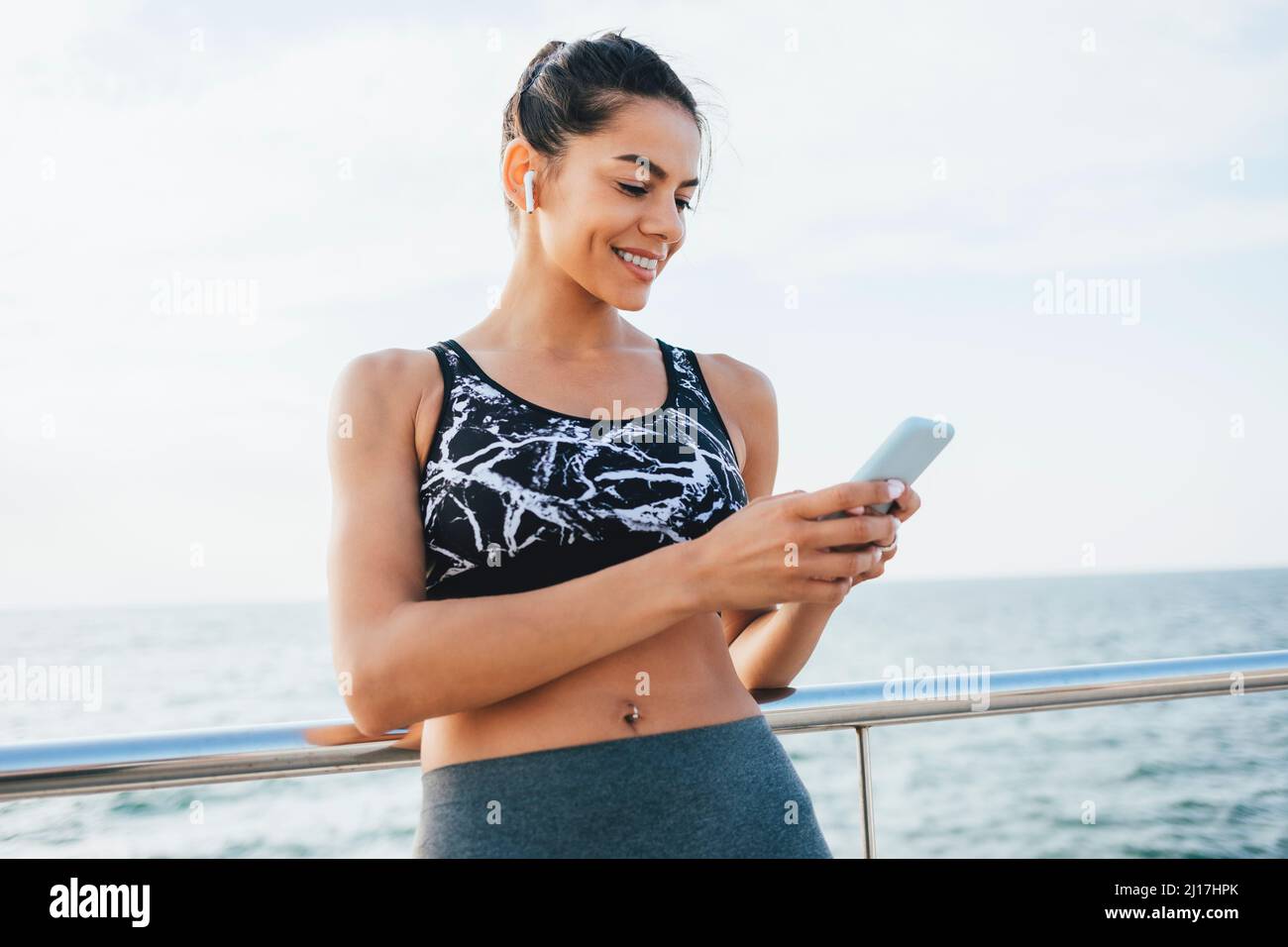 Felice giovane donna surf rete attraverso il cellulare in piedi da ringhiera Foto Stock
