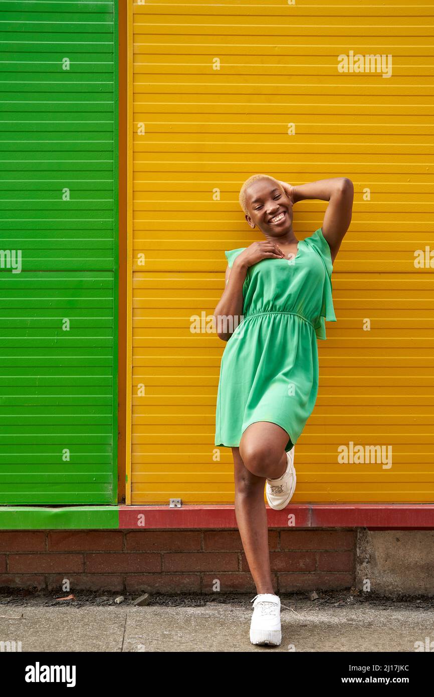 Donna felice in piedi su una gamba di fronte al muro verde e giallo Foto Stock