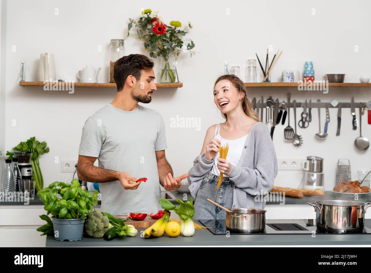 Giovane uomo che parla con una ragazza felice che tiene la pasta in piedi in cucina a casa Foto Stock