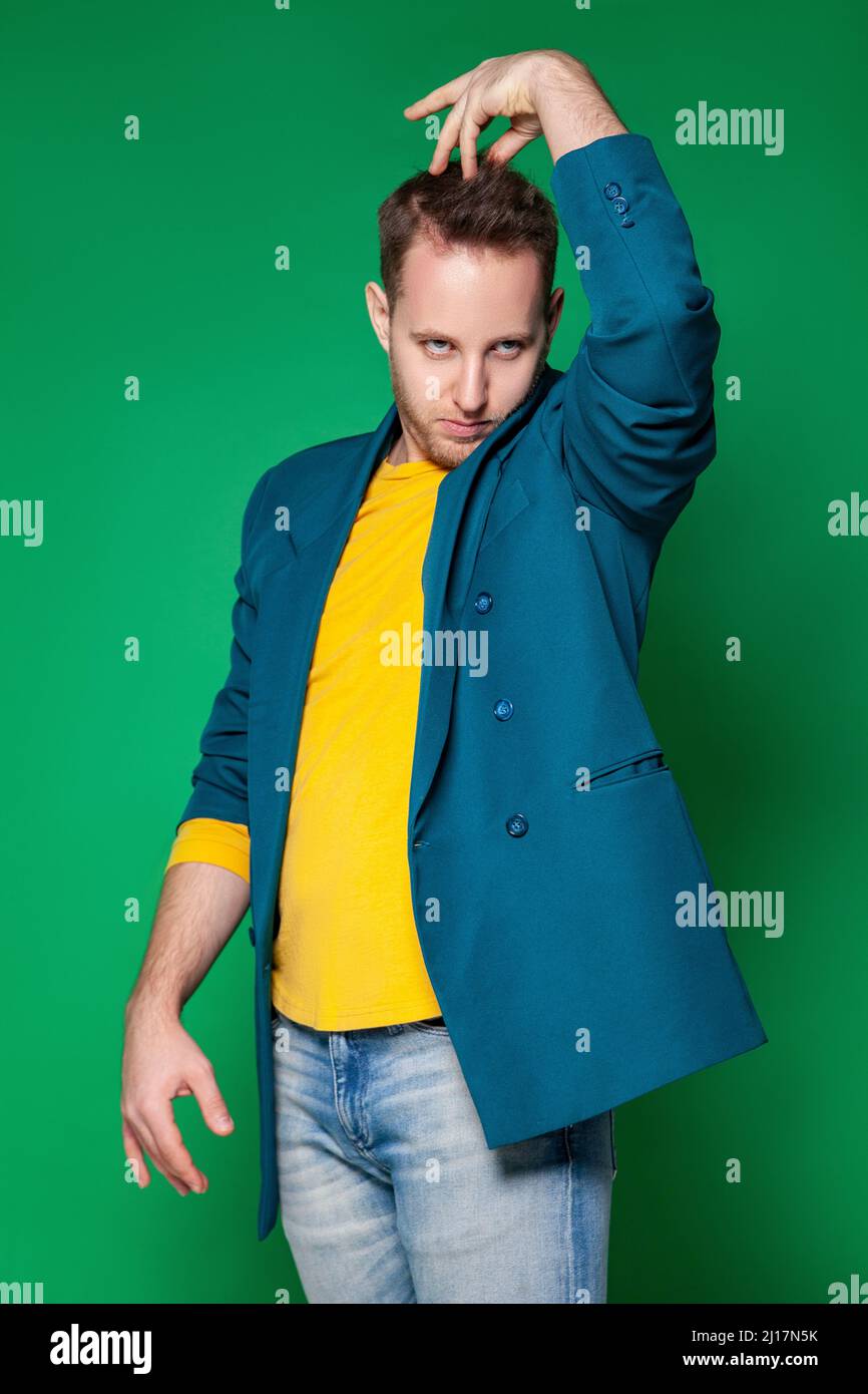 Giovane uomo divertente che tocca i capelli in piedi su sfondo verde Foto Stock