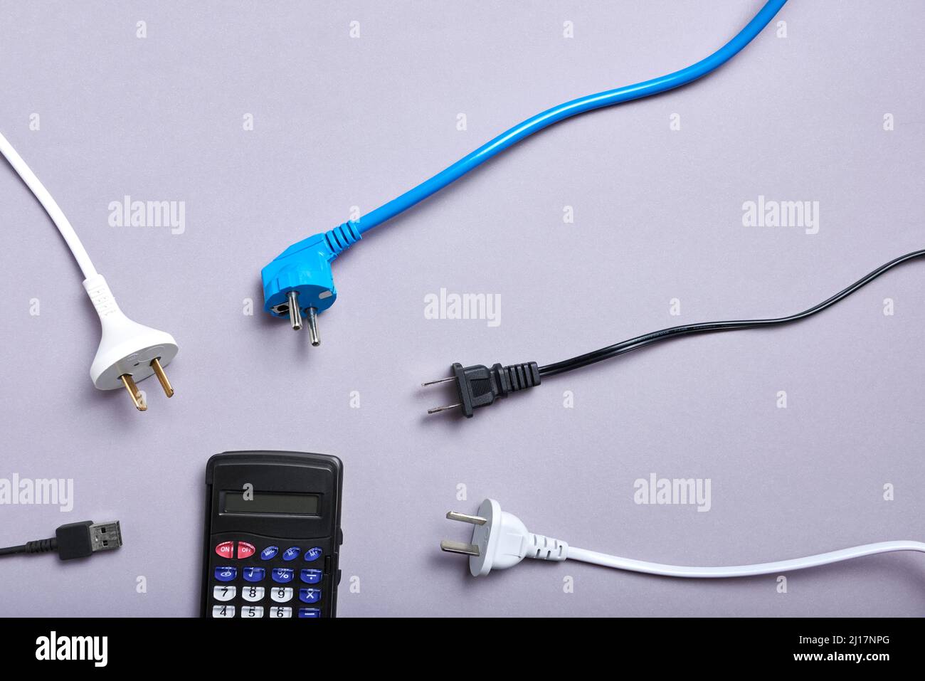 Immagine concettuale sull'elevato costo economico dell'energia elettrica e sull'aumento dei tassi di energia: Cavi di alimentazione che circondano una calcolatrice. Foto Stock