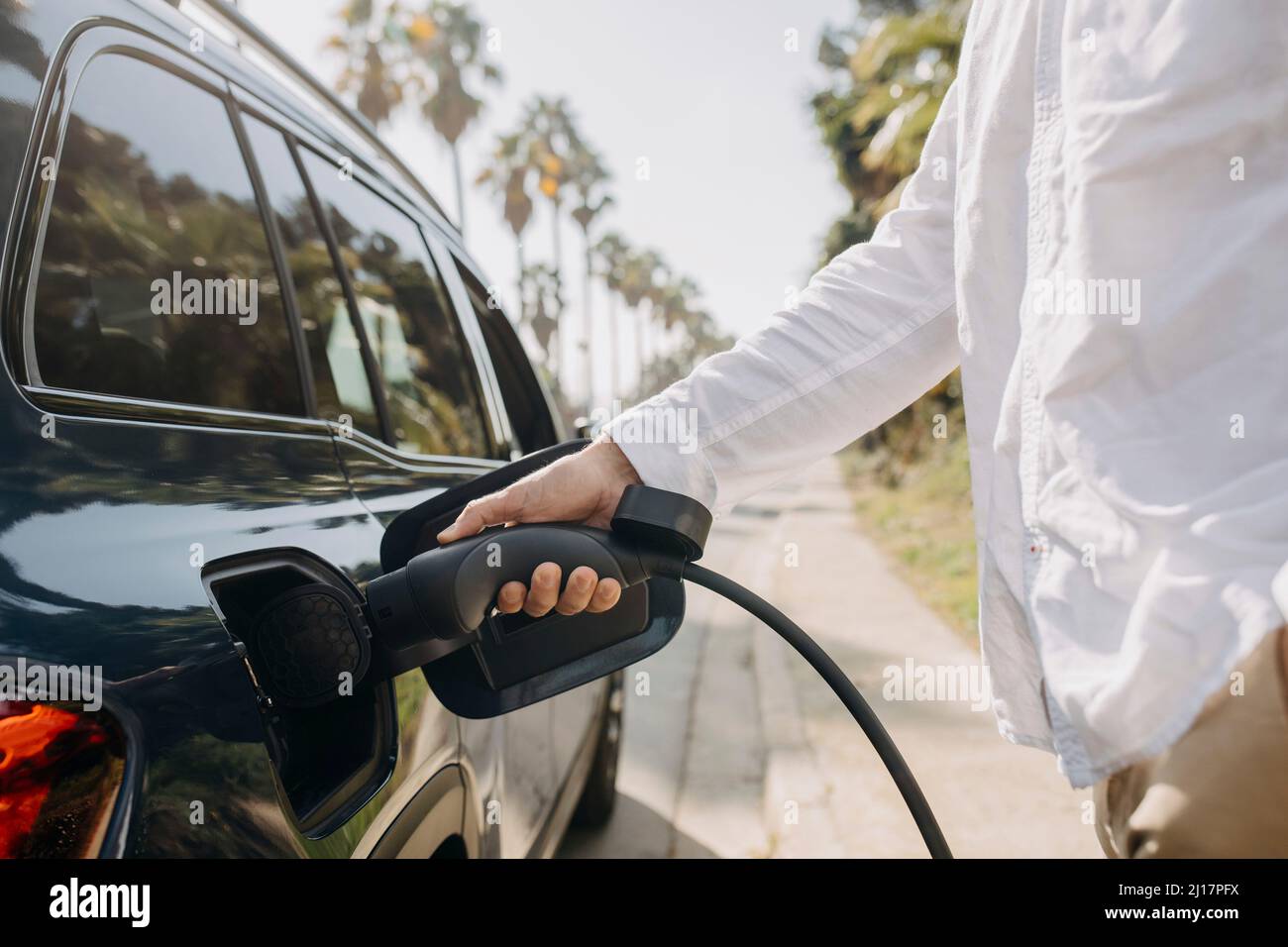 Uomo che collega il cavo di ricarica all'auto elettrica sulla strada alla stazione Foto Stock