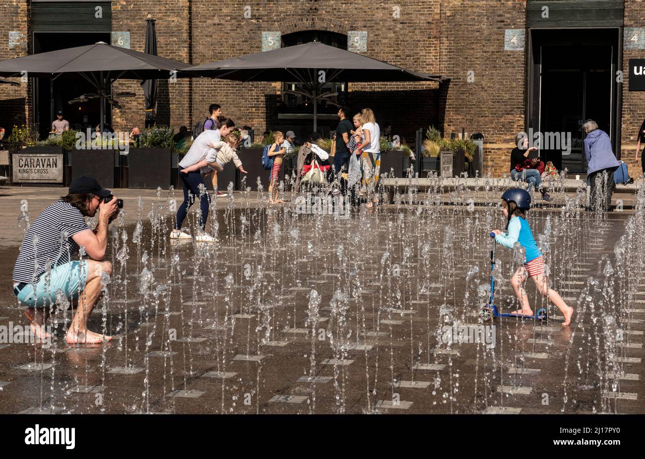Londra, Regno Unito. 23rd Mar 2022. Un giovane ragazzo si raffredda correndo attraverso la fontana di Piazza Granary con il suo scooter mentre le temperature raggiungono ancora oggi i 20 gradi nella capitale. Picture Credit: ernesto Rogata/Alamy Live News Foto Stock