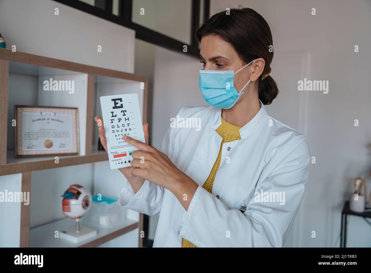 Medico con maschera protettiva che mostra il diagramma degli occhi in clinica Foto Stock