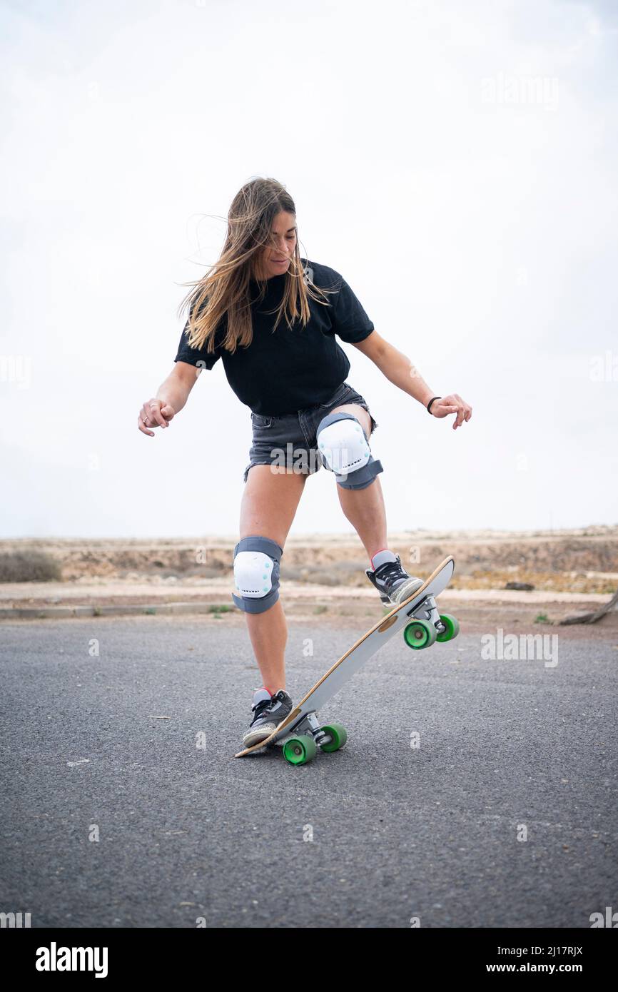 Giovane donna che mostra abilità con skateboard su strada Foto Stock