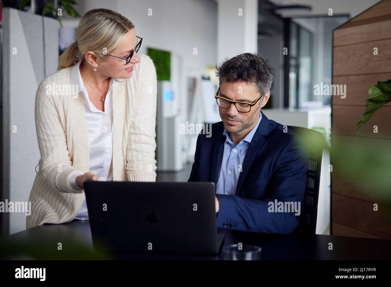 Donna d'affari che condivide idee con un collega seduto alla scrivania in ufficio Foto Stock