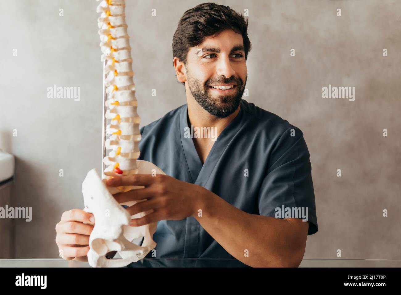 Giovane fisioterapista sorridente con modello di colonna umana in clinica medica Foto Stock