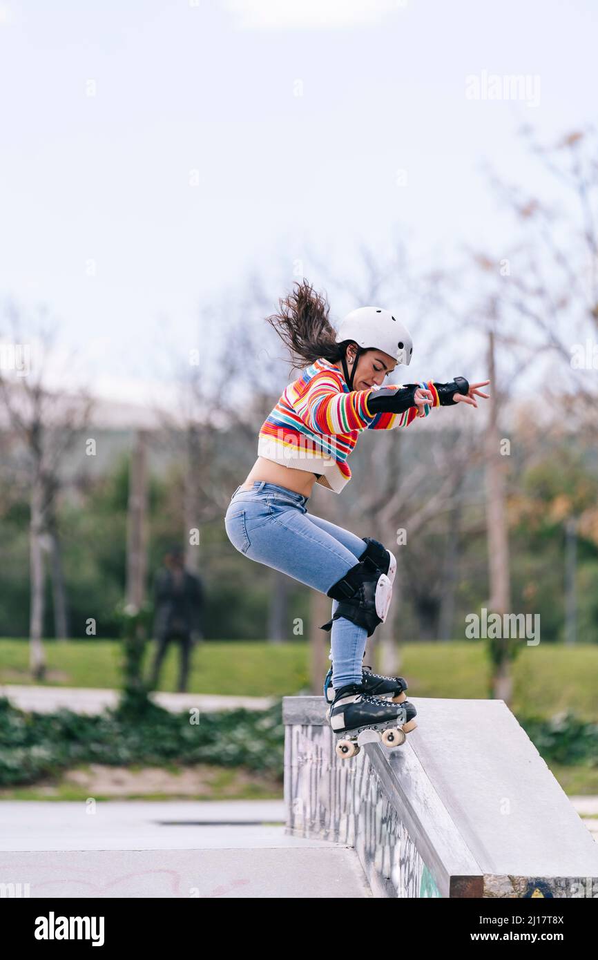 Donna che mostra abilità con pattinaggio a rotelle su ringhiera al parco skateboard Foto Stock