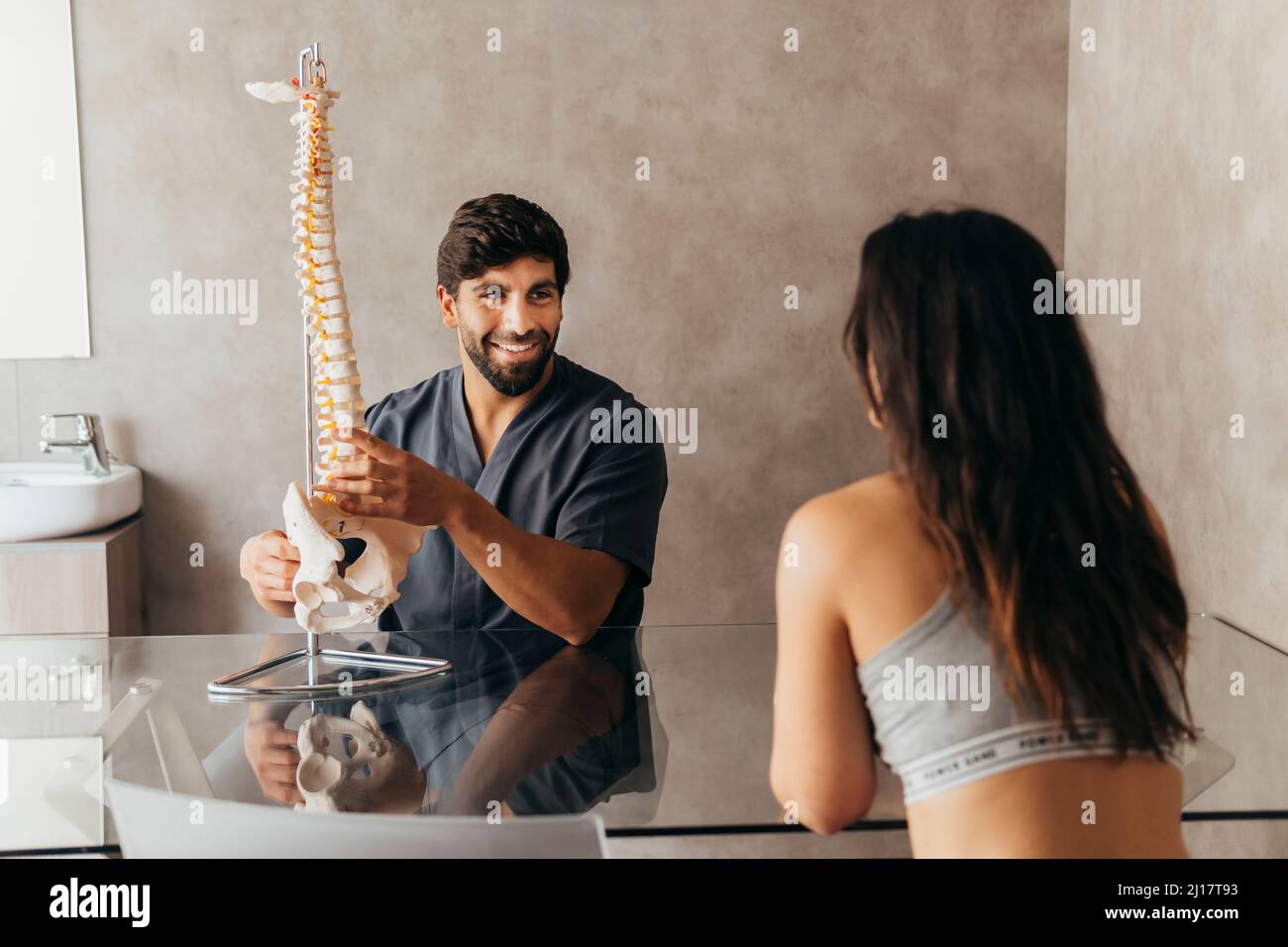 Fisioterapista sorridente che spiega l'anatomia della spina umana alla donna Foto Stock