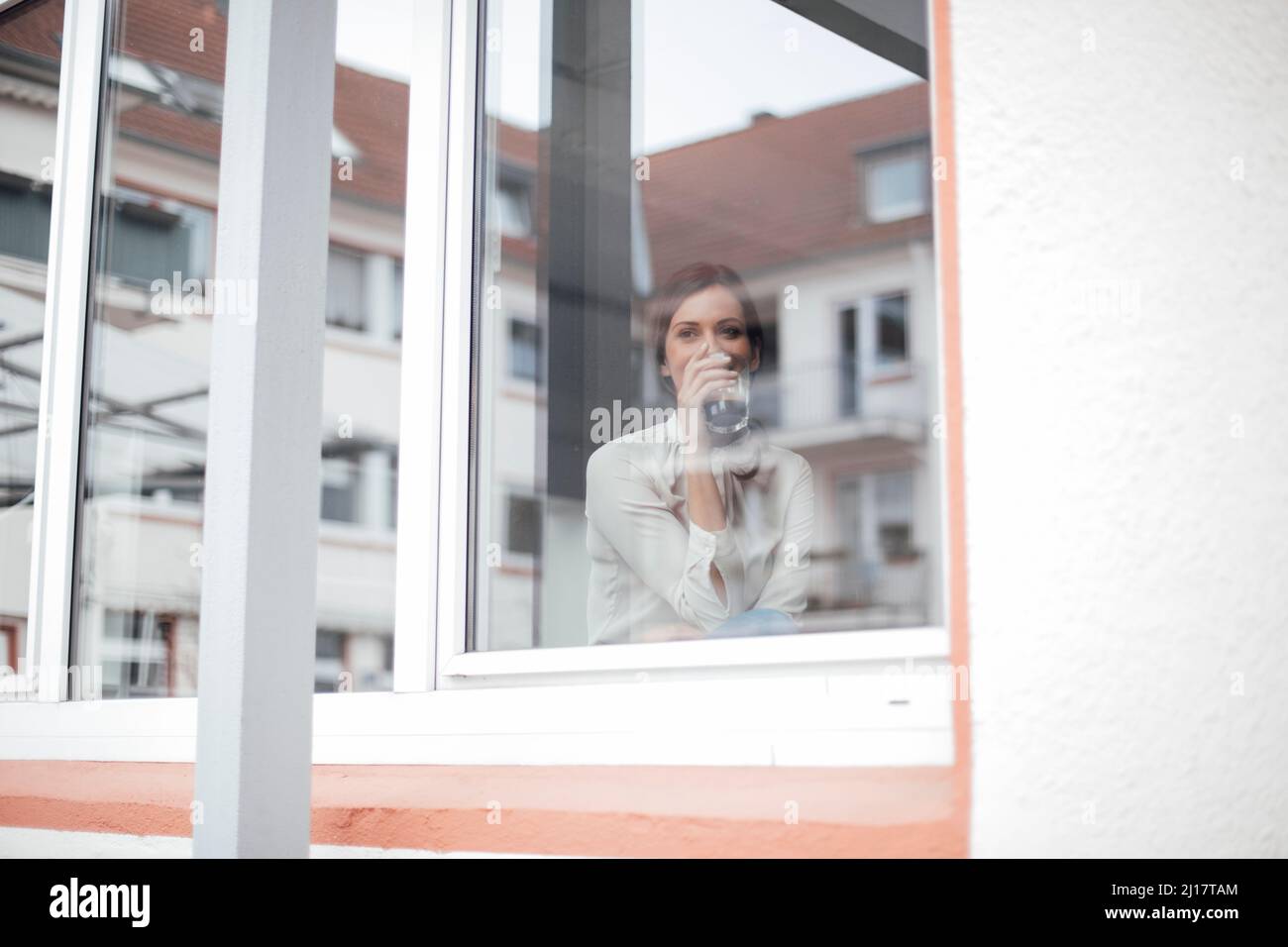 Donna d'affari che beve il caffè visto attraverso la finestra di vetro Foto Stock