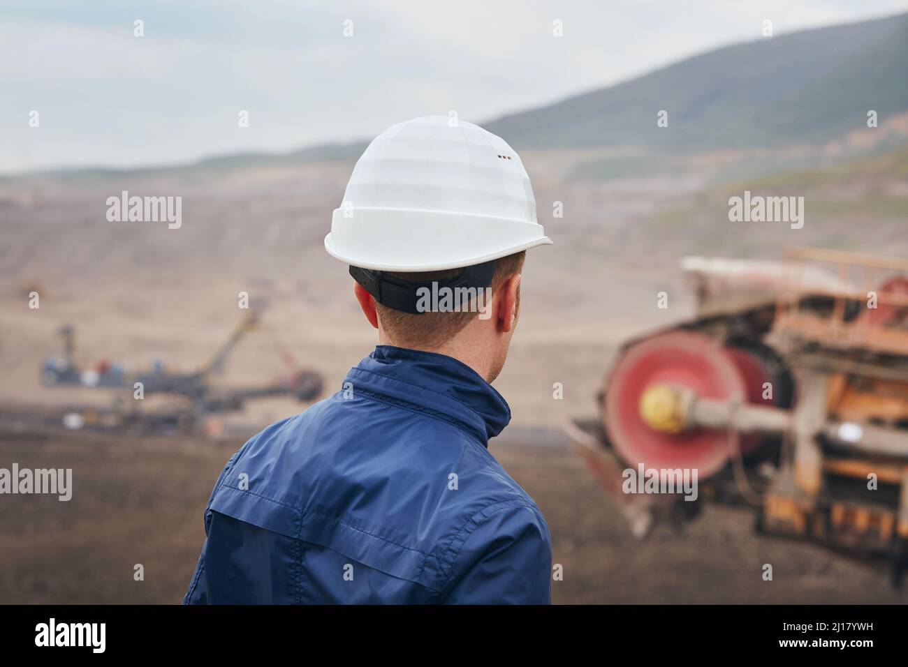 Estrazione di carbone in miniera di superficie. Minatore che guarda sull'escavatore enorme. Foto Stock