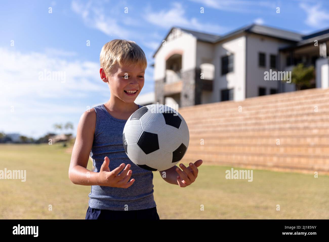 Sorridendo scolaro caucasico elementare giocando con la palla di calcio sul campo contro l'edificio scolastico Foto Stock