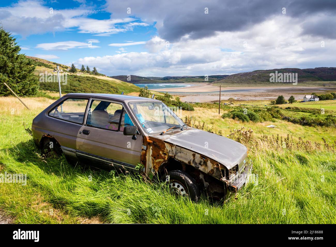 L'erba cresce intorno ad un'auto abbandonata, una Ford Fiesta, dietro la quale si trova l'ampia spiaggia di Torrisdale in Scozia. Foto Stock