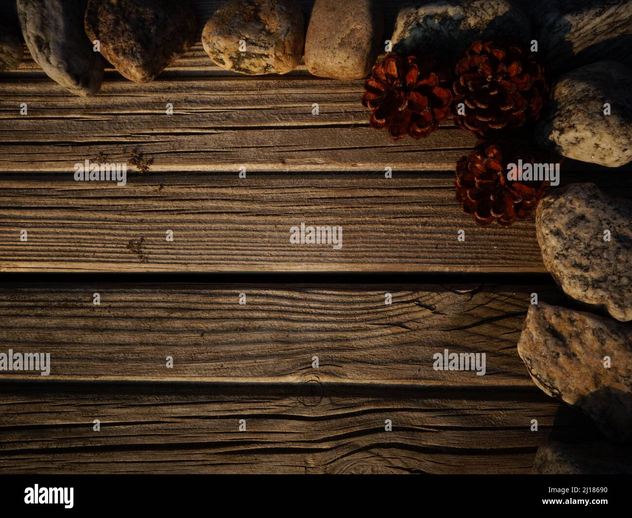 Cornice angolare decorativa di pietre e coni di pino su pavimenti in legno, adatta come sfondo per aggiungere testo ad un invito, un segno naturale. Foto Stock