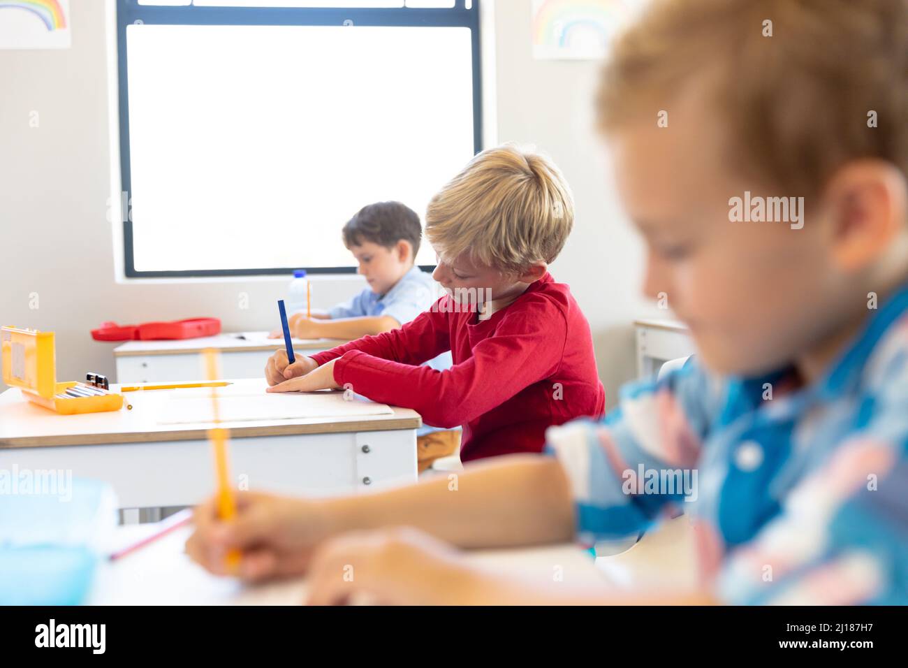 Ragazzi di scuola elementare multirazziale scrivono sui libri mentre si siedono alla scrivania in classe Foto Stock