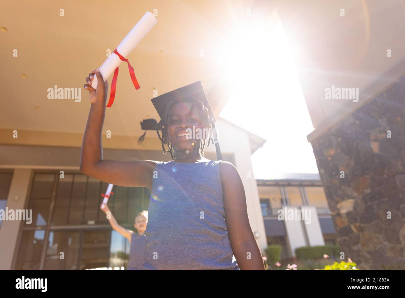 Ritratto di scolaro elementare afroamericano con mortarboard che mostra grado in giorno di sole Foto Stock