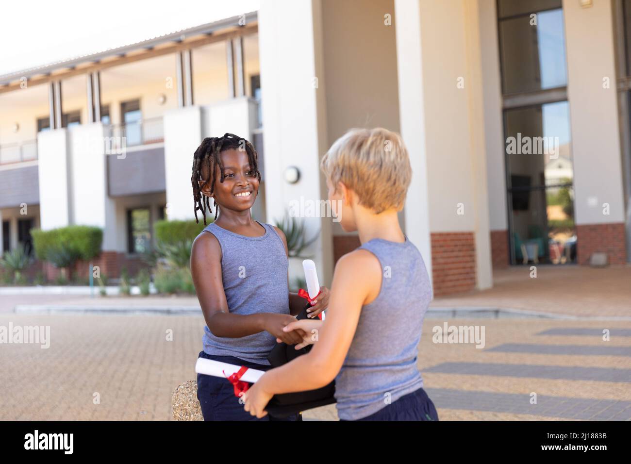 Ragazzi di scuola elementare afro-americani e caucasici con diploma e ipoteca che fanno handshake Foto Stock