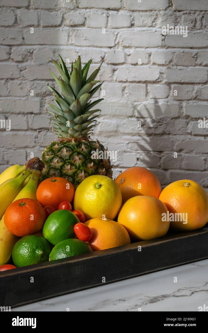 Un assortimento di frutta su un vassoio nero su uno sfondo di mattoni Foto Stock