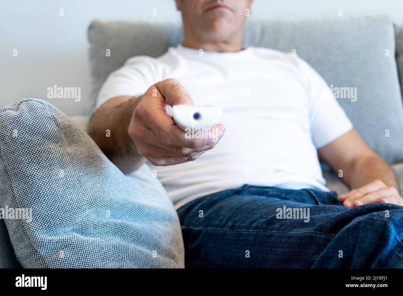 Uomo non riconosciuto che punta con il telecomando del televisore dal divano con la messa a fuoco sulla mano Foto Stock