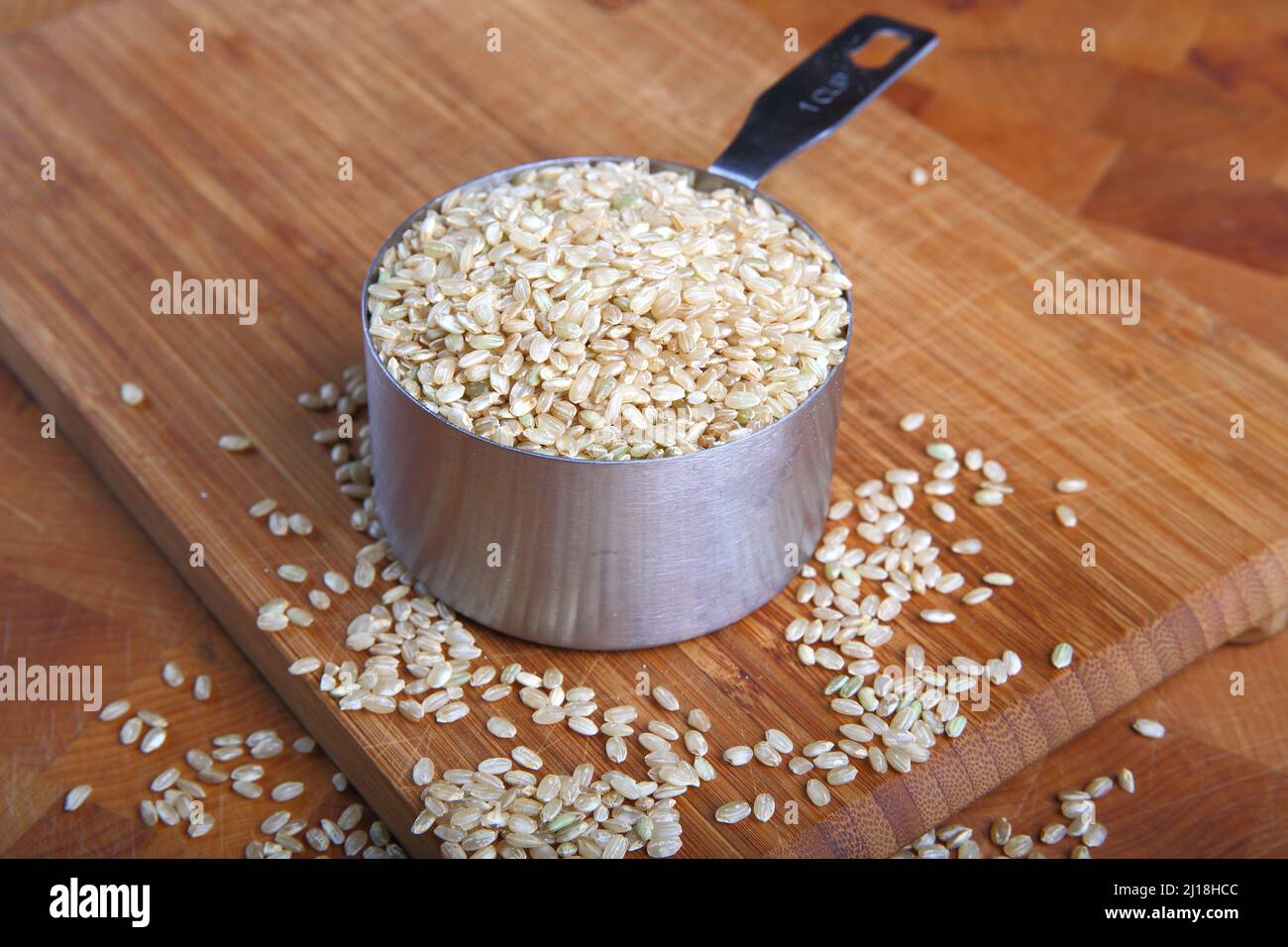 Riso marrone e misurino su sfondo di legno Foto Stock