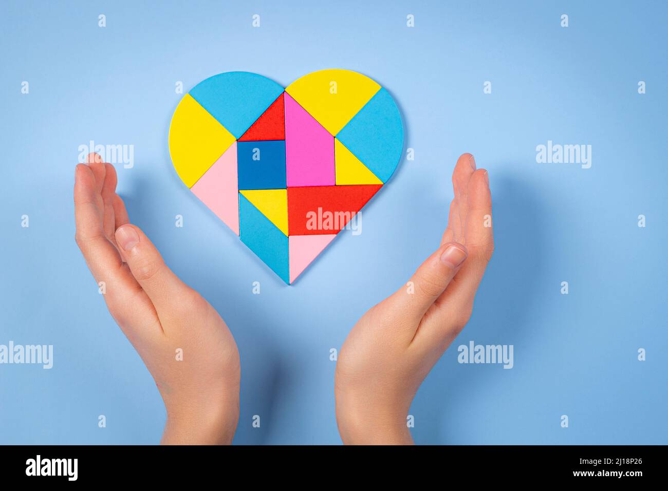 Mani del bambino con cuore colorato del puzzle su sfondo azzurro chiaro. Concetto di giornata di consapevolezza autismo mondiale Foto Stock